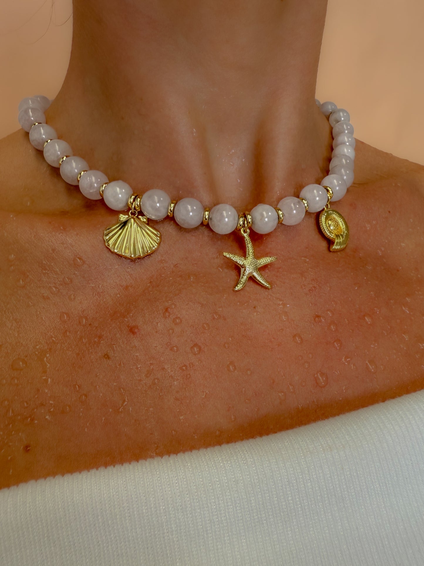 Crystal beaded necklace with shell and starfish charms on a neck against a neutral background